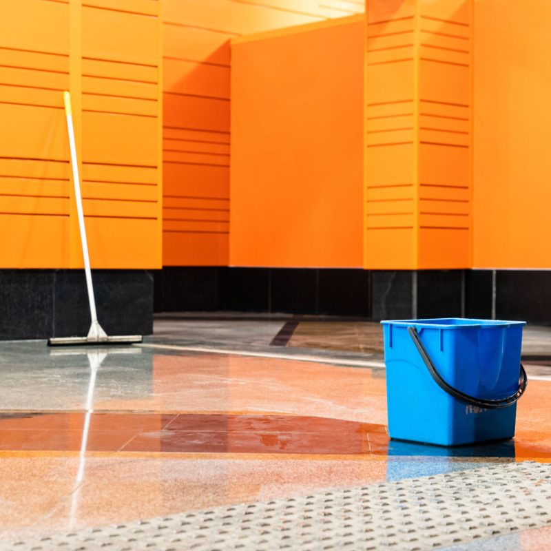 Disinfection of subway stations during the coronavirus pandemic. Blue plastic bucket and mop against the background of an empty station with orange walls.