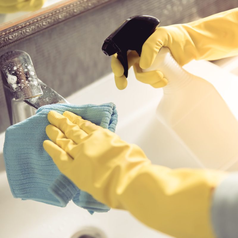 Cropped image of beautiful young woman using a duster and a detergent while cleaning sink and tap in bathroom