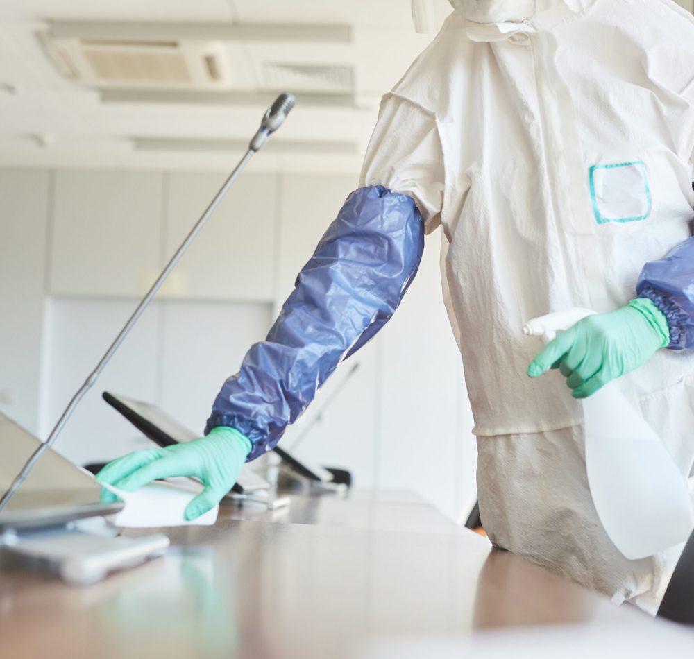 Cropped portrait of sanitation worker wearing hazmat suit cleaning and disinfecting conference room in office, copy space